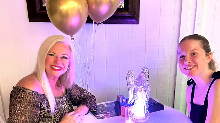 Michael Sue Scott Intuitive Reader smiles with a teenager and gold and pink balloons with an angel sculpture and Tarot Cards